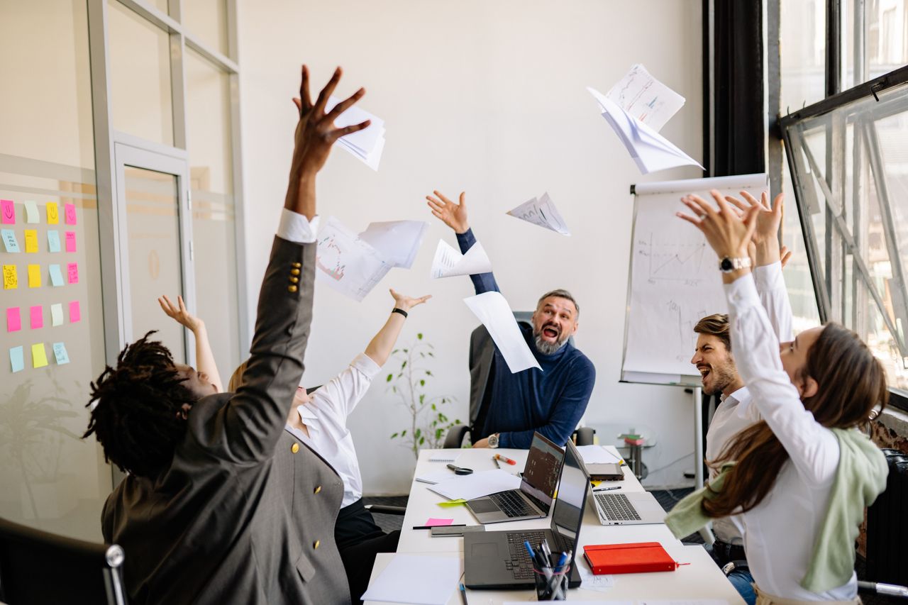 Home A diverse office team celebrating with papers in the air, showing teamwork and success.